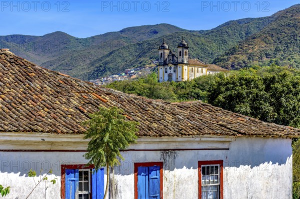 Old weathered colonial house with a baroque church and mountain in the background in the historic city of Ouro Preto, Ouro Preto, Minas Gerais, Brazil