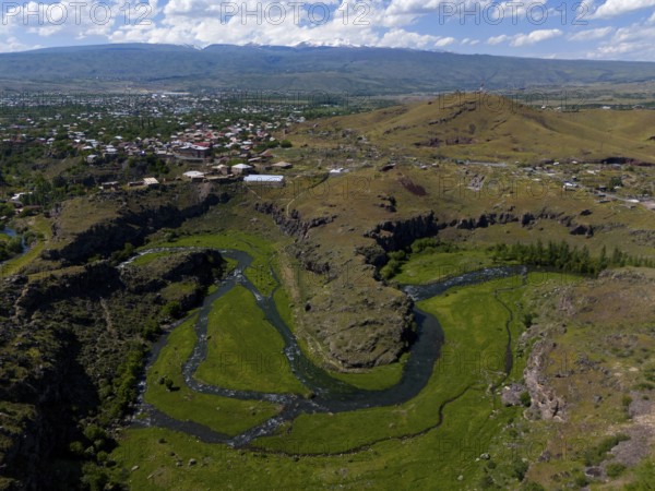 A river meanders through green landscapes with a city in the background and hills in the distance, aerial view, Kassagh River, Oskahan, Oshakan, Ošakan, Aragazotn Province, Armenia