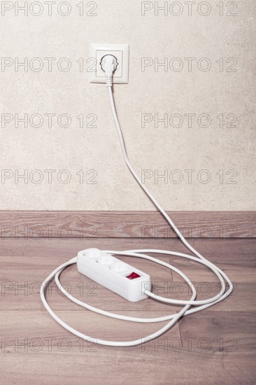 Electrical power strip connected to wall outlet on wooden floor in bright room