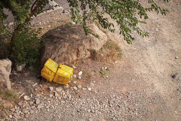 08/25/2025 Georgia, Tbilisi, Delivery packages, Glovo company, left on stony ground, near bushes, outdoors, no people