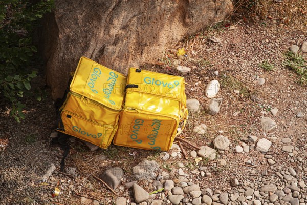 08/25/2025 Georgia, Tbilisi, Delivery packages, Glovo company, left on stony ground, near bushes, outdoors, no people