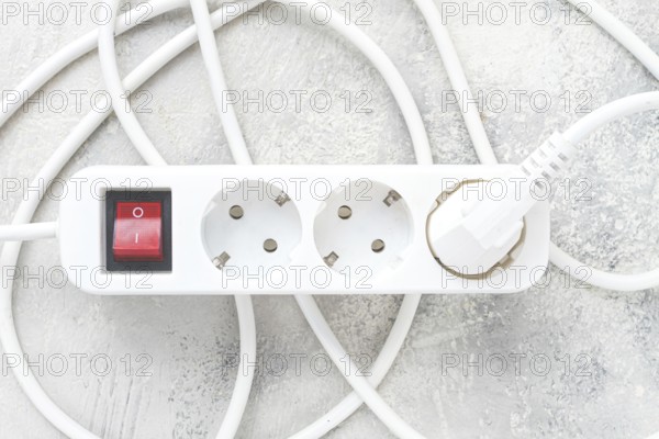 Power strip with multiple sockets and a switch in a cluttered setup on a textured surface during daytime