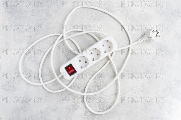 Power strip with multiple sockets and a switch in a cluttered setup on a textured surface during daytime