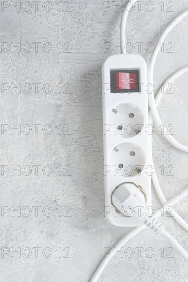 Power strip with multiple sockets and a switch in a cluttered setup on a textured surface during daytime
