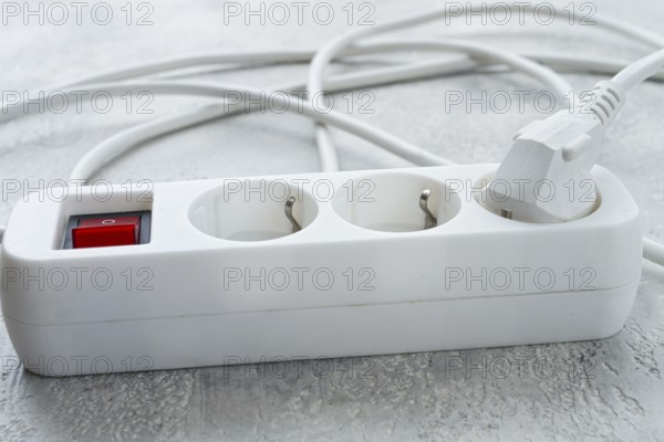 Power strip with multiple sockets and a switch in a cluttered setup on a textured surface during daytime