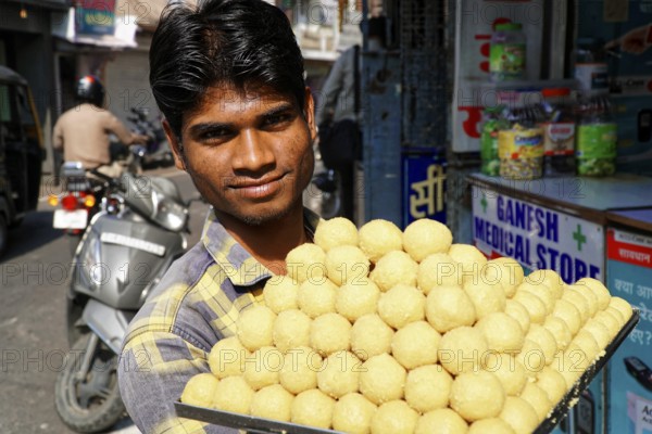Udaipur, Rajasthan, North India, Asia, A vendor offers a platter full of traditional Indian laddus and smiles