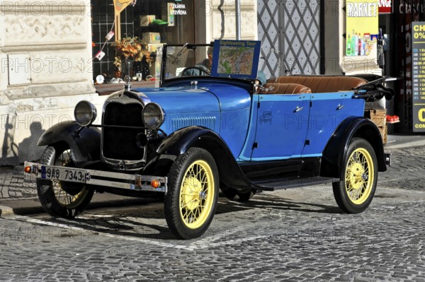Prague, Czech Republic, Europe, Blue vintage car with yellow wheels parked on the pavement in front of shops