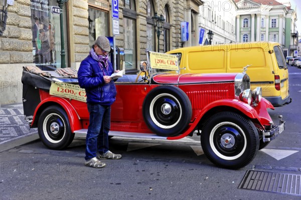 Prague, Czech Republic, Europe, Man reading in front of a classic red vintage car on a busy street in Prague