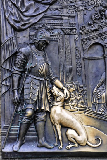 Tourists touch a plaque that is part of the statue of St John of Nepomuk and is supposed to bring good luck, Prague, bronze figure of a knight stroking a dog, artistically designed, Prague, Czech Republic