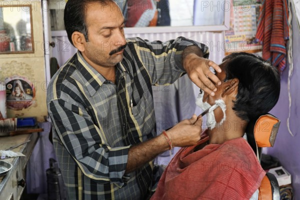 Kota, Rajasthan, North India, Asia, A barber shaves a customer's face in a small hairdressing salon, India