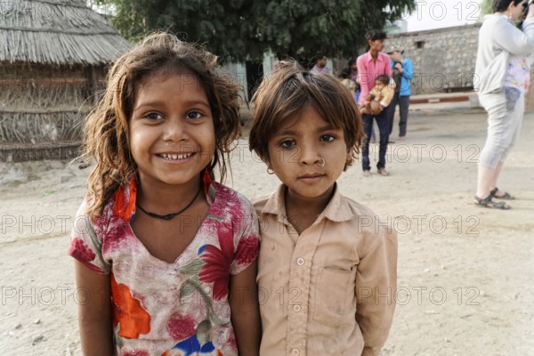 Sawai Madhopur, Kota, Rajasthan, North India, Asia, Two children smiling friendly, a village in the background. Girl in colourful and beige clothes, India