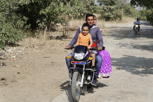 Kota, Rajasthan, North India, Asia, Family riding a motorbike along a rural road in sunny weather, India