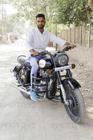 Kota, Rajasthan, North India, Asia, Man sitting on a black Royal Enfield motorbike on a dusty road, India