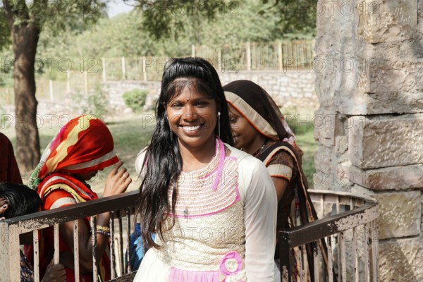 Kota, Rajasthan, North India, Asia, Smiling woman in bright traditional dress in front of a stone wall, India