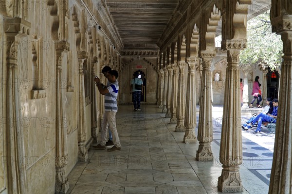 City Palace, Udaipur, Rajasthan, India, Asia, A long corridor decorated with stone carvings and people in a historic Indian building, North India