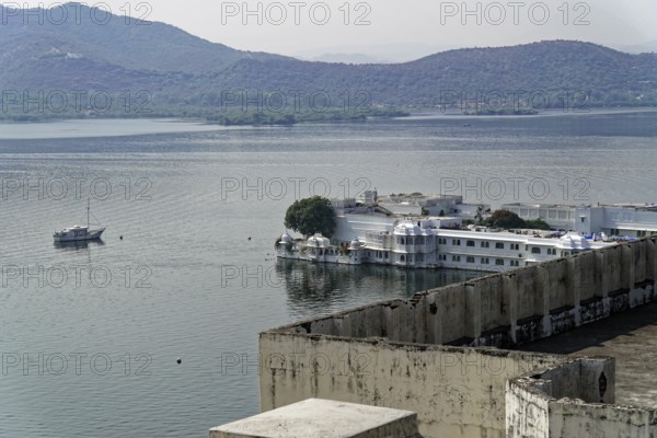 Tranquil scene with lake, boat and mountains in the background, including a building by the water, Udaipur, Rajasthan, North India