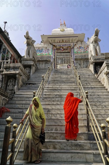 Entrance to Jagdish Temple, Udaipur, people climb the steps to a temple, flanked by statues under a clear sky, Rajasthan, North India, India, Asia, Women in saris climb the stairs of a traditional temple, flanked by elephant statues