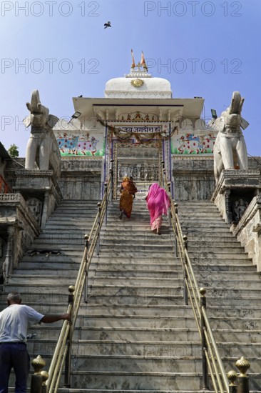 Entrance to Jagdish Temple, Udaipur, People climbing the steps to a temple flanked by statues under a clear sky, Rajasthan, North India, India, Asia, Traditional temple with detailed staircase, wall art and elephant statues, under a clear sky with two people