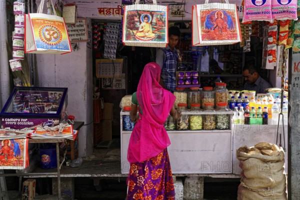 Udaipur, Rajasthan, North India, India, Asia, A woman in traditional dress looks at goods at a colourful market stall