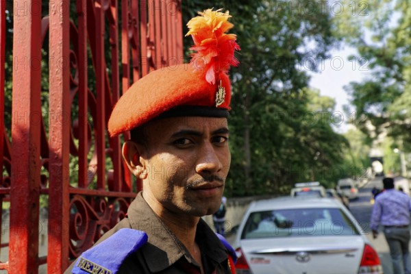 Udaipur, Rajasthan, North India, India, Asia, A guard in uniform with a red beret poses in front of a red lattice gate