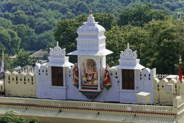 City Palace, Udaipur, Rajasthan, India, Asia, Traditional temple building with decorative statue and green forest backdrop, North India