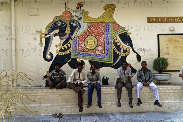 Udaipur, Rajasthan, North India, Asia, Several men sitting in front of an artistically painted elephant mural