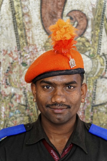 Udaipur, Rajasthan, North India, Asia, A man in uniform with an orange cap smiles in front of a patterned background