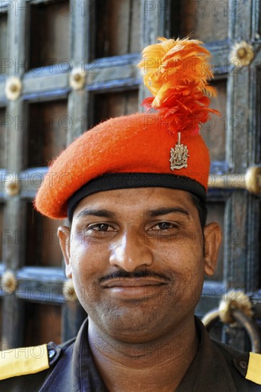 Udaipur, Rajasthan, North India, Asia, A man in uniform with an orange cap and feather smiles in front of a lattice door