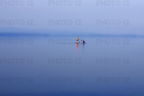 A calm lake (Steinhuder Meer) with paddleboarders under a blue and wide sky, Wunstorf