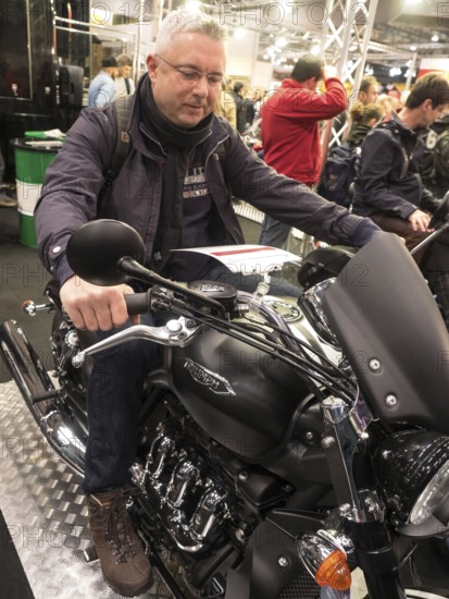 Man sitting on a Triumph motorbike, surrounded by trade fair visitors, dortmund, deutchland