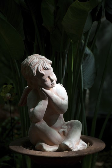 Stone sculpture of a pensive angel in a dark, shady garden, südlohn, westphalia, germany
