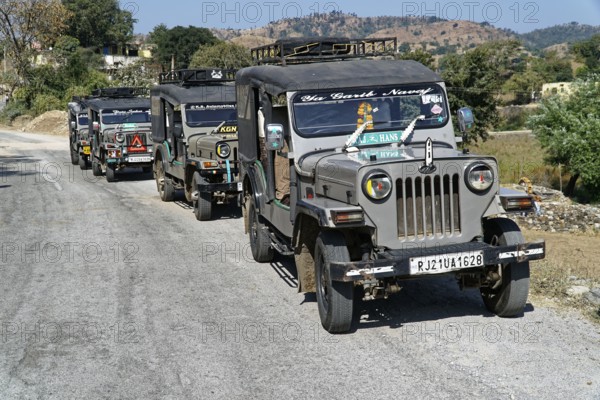 A convoy of jeeps drives along a country road in a mountainous region, Ranakpur, Jodhpur, Rajasthan, North India