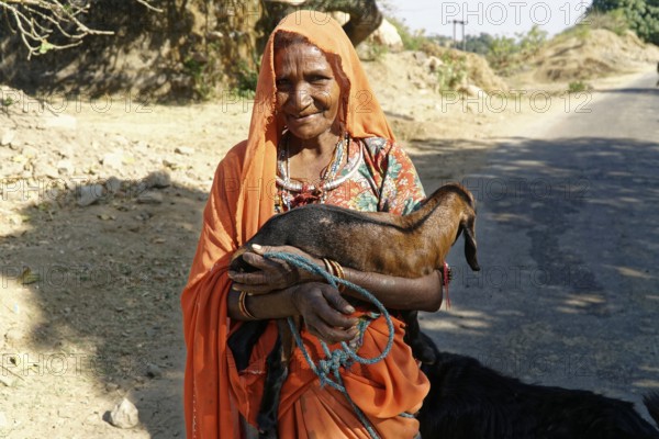Elderly woman in traditional dress holding a goat in a rural area, Ranakpur, Jodhpur, Rajasthan, North India
