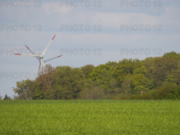 A wind turbine behind green trees and meadows under a cloudy sky, weseke, münsterland, germany