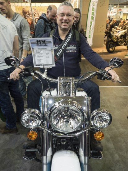 Smiling man sitting on a motorbike during a trade fair and enjoying himself, dortmund, germany