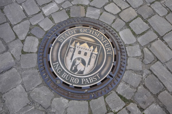 Round manhole cover with town coat of arms and inscription, paving stones, ground, Ochsenfurt, Lower Franconia, Franconia, Bavaria, Germany
