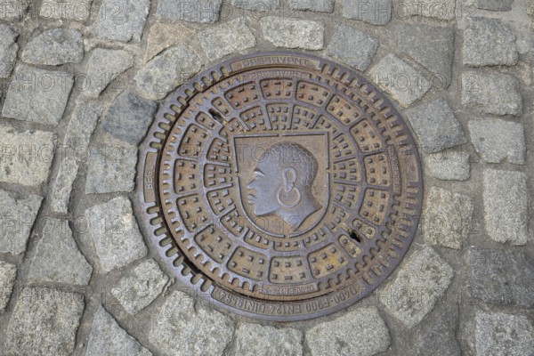Round manhole cover with city coat of arms, inscription, cobblestones, floor, head, African, earring, Coburg, Upper Franconia, Franconia, Bavaria, Germany