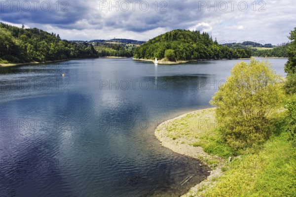 A lake (Aggertalsperre) with a wooded island and trees on the shore under a summer sky, Bergneustadt