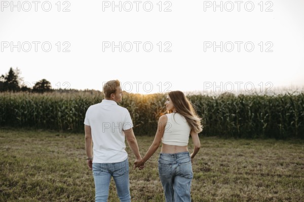 Couple walking hand in hand across a mown field