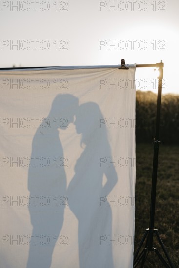 Pregnant young woman with partner in silhouette behind a sheet