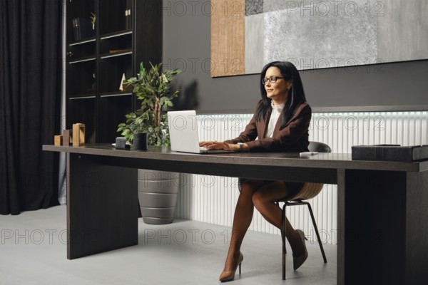 A business professional typing a report on her laptop while seated at a sleek desk in a contemporary office