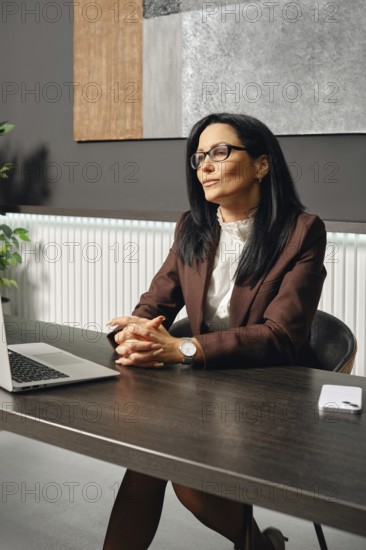 A serious female divorce lawyer listens to her interlocutor with a smile over a video link. She knows the best solution to the problem in a contemporary office