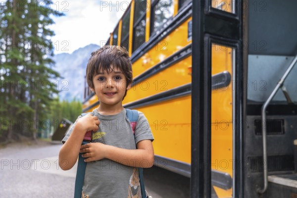 Happy elementary school student carrying backpack is waiting for the school bus in a mountain location, ready for his first day back to school