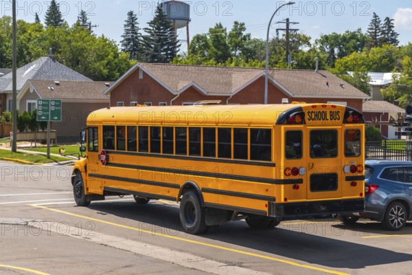 Yellow school bus driving down a suburban street during the daytime, transporting students to or from school, highlighting the importance of safe and reliable transportation in education