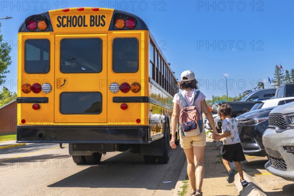 Mother holding son's hand walking towards a school bus on the first day back to school, representing the start of a new academic year and childhood education