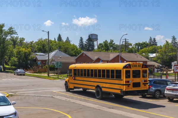 Classic yellow school bus driving away from an intersection in a quiet residential area, marking the end of the school day under a clear blue sky