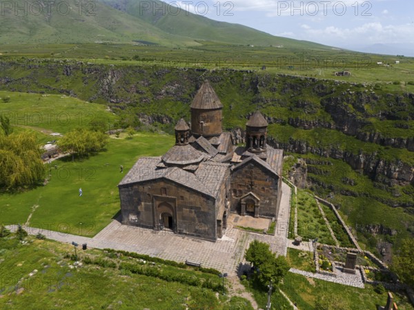 Historic stone church on a green plain in front of a mountain landscape under a blue sky, aerial view, Saghmosavank Monastery, Saghmosavank, Saghmosavank, Salmosavank, Aragazotn Province, Armenia