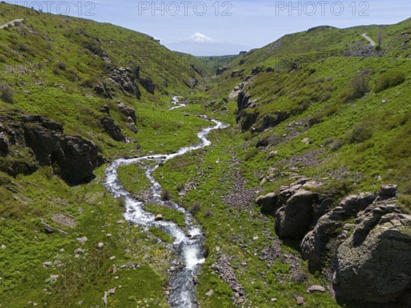A winding river meanders through a green gorge with a view of a distant snow-capped mountain, aerial view, river and gorge Arkashian, in the background Mount Ararat in Turkey, Aragazotn province, Armenia