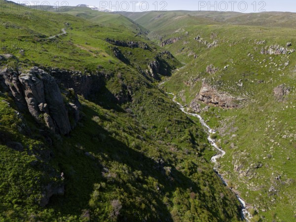 A deep gorge with a river surrounded by green hills under a clear blue sky, aerial view, river and gorge Arkashian, Aragazotn province, Armenia
