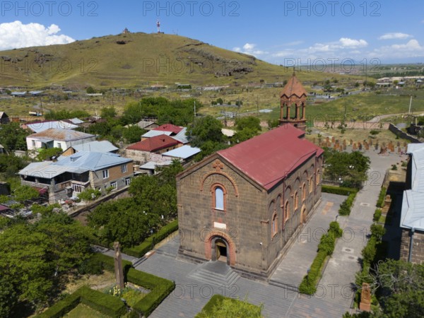Small brick church in a rural setting with a nearby hill and blue sky, aerial view, Church of St Mesrop Mashtots, Mesrop Mashtots Church, Oskahan, Oshakan, Ošakan, Aragazotn Province, Armenia